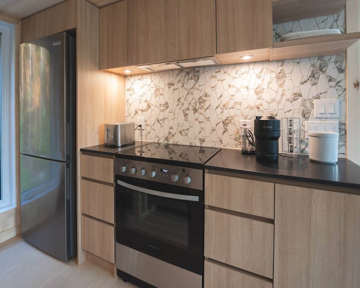 Une cuisine moderne dotée d’un réfrigérateur en acier inoxydable, d’une cuisinière noire, de meubles en bois et d’un dosseret en marbre.