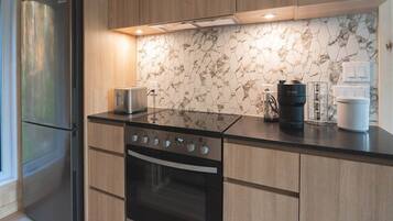Une cuisine moderne dotée d’un réfrigérateur en acier inoxydable, d’une cuisinière noire, de meubles en bois et d’un dosseret en marbre.