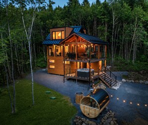 A two-story log cabin with a deck, outdoor seating, and a barrel.