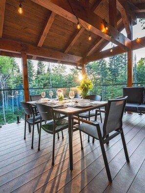 Ein Essbereich im Freien mit einer Holzterrasse, einem Tisch für vier Personen und Blick auf den Wald.