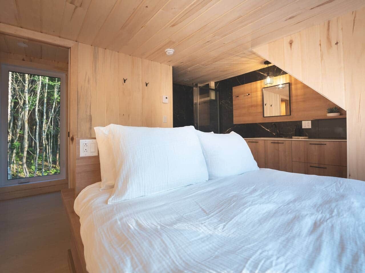 Ein Schlafzimmer mit einem großen Bett, einem Fenster mit Blick auf Bäume und einer Küchenzeile mit Holzschränken.