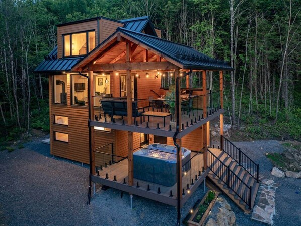A two-story cabin with a balcony, a hot tub, and a staircase leading to the upper level.