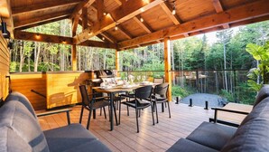 An outdoor wooden deck with a dining table and chairs, surrounded by a wooden railing, overlooking a forested area. - MAO / Micro-Chalet / Private Thermal Experience near Quebec (Capitale-Nationale)