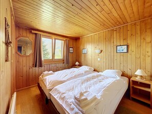 Une pièce aux murs lambrés, avec deux lits, une fenêtre et un miroir.