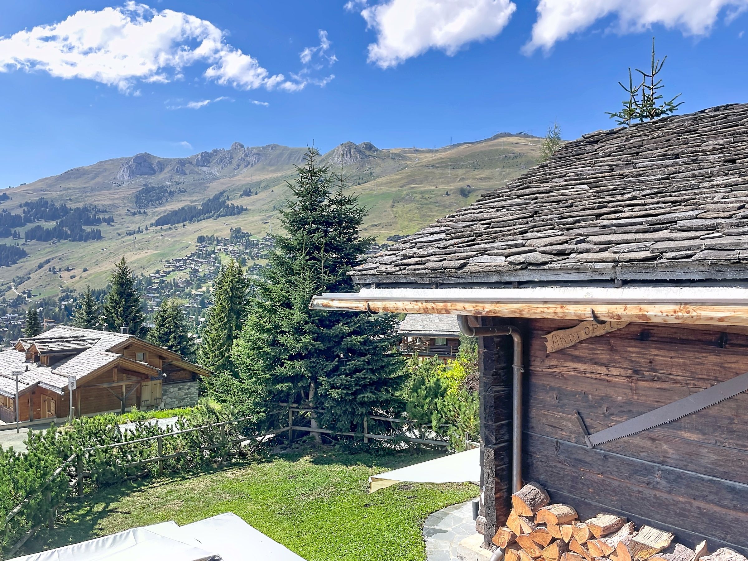 A wooden cabin with a sloped roof, surrounded by a well-maintained lawn and a view of a mountain range.
