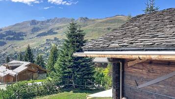 A wooden cabin with a sloped roof, surrounded by a well-maintained lawn and a view of a mountain range.