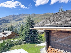 Une cabane en bois avec un toit en pente, entourée d’une pelouse bien entretenue et offrant une vue sur une chaîne de montagnes.