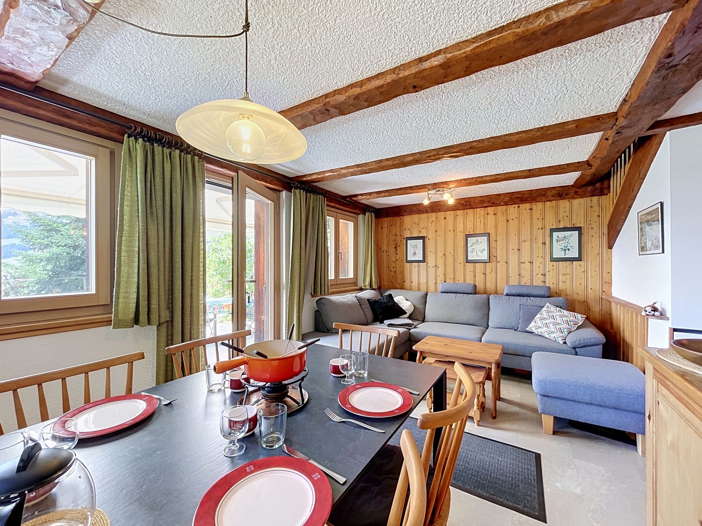 Un coin repas avec une table dressée pour quatre personnes, un canapé et un plafond en bois.