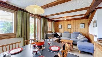 Un coin repas avec une table dressée pour quatre personnes, un canapé et un plafond en bois.