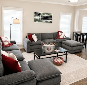 A living room with a sectional sofa, a coffee table, a lamp, and a baseball-themed decor.