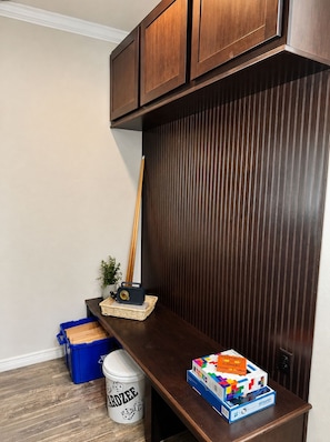 A corner of a room with a dark wooden cabinet, a blue storage bin, a white bucket labeled 'CARDZEE,' and a box of 'Millennials Zoomers' puzzle.