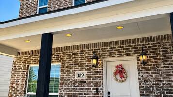 Un bâtiment en briques de deux étages, avec une porte d'entrée blanche, le numéro « 109 » au-dessus de la porte, et un porche agrémenté d'un banc et d'une petite décoration en forme de citrouille.