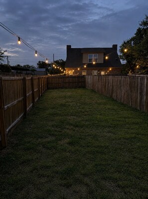 A backyard with a wooden fence, a house, and string lights.
