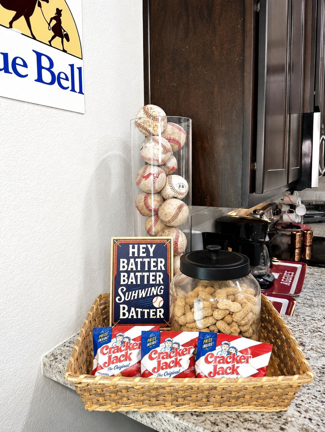 A kitchen counter with a glass jar of baseballs, a sign reading 'Hey Batter, Suhwings Batter,' and a basket of Cracker Jack snacks.
