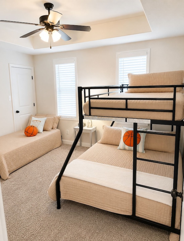 A bunk bed room with a ceiling fan, a door, and two windows with blinds.
