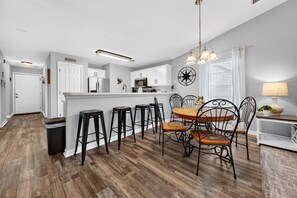 A modern kitchen with white cabinets, a central island, and a dining area with a round table and chairs. - SeaShell Escape, Pool , Hot Tub & Golf Getaway (Pawleys Island)