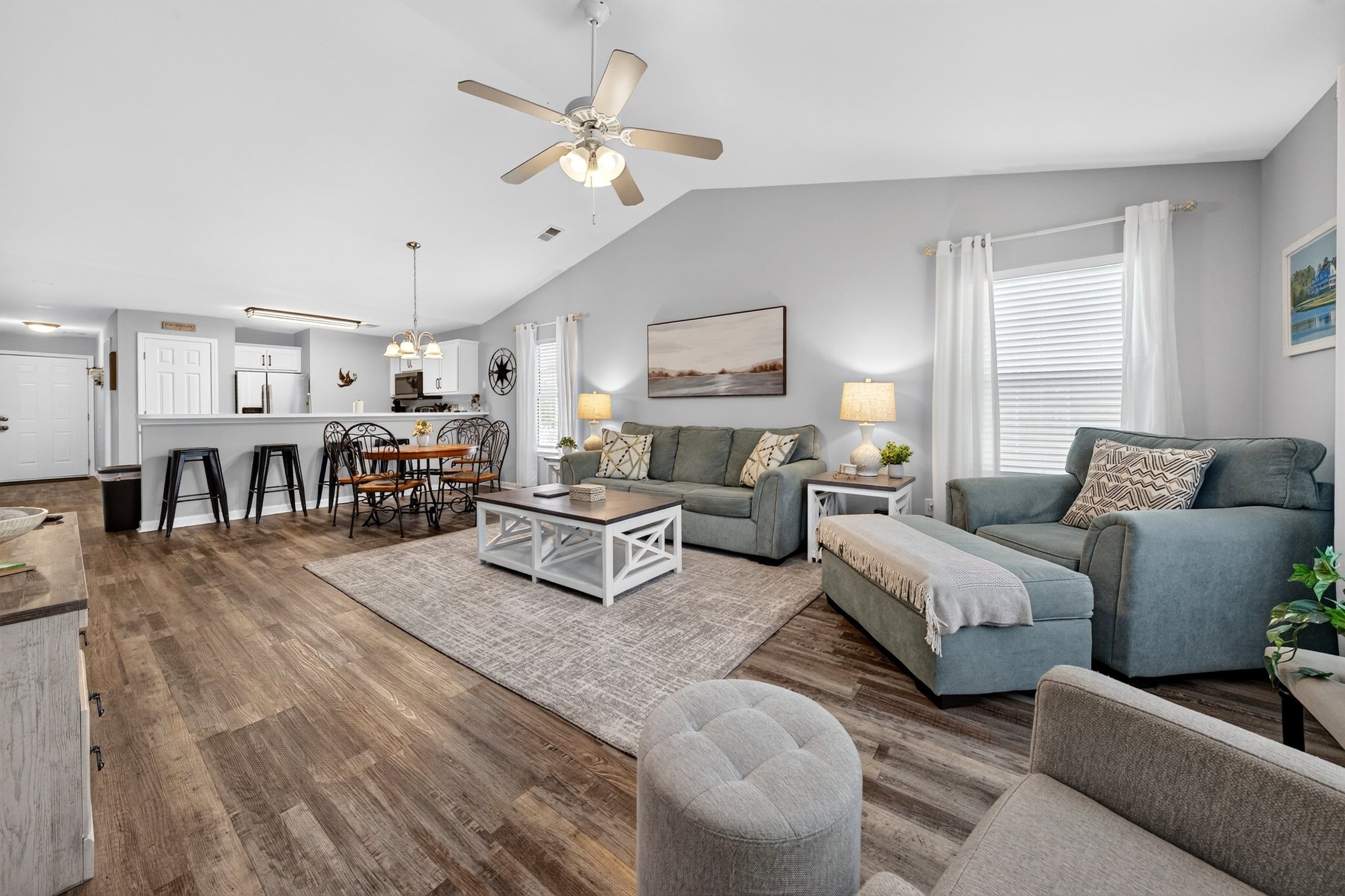 A spacious living area with a dining table, sofas, and a ceiling fan.