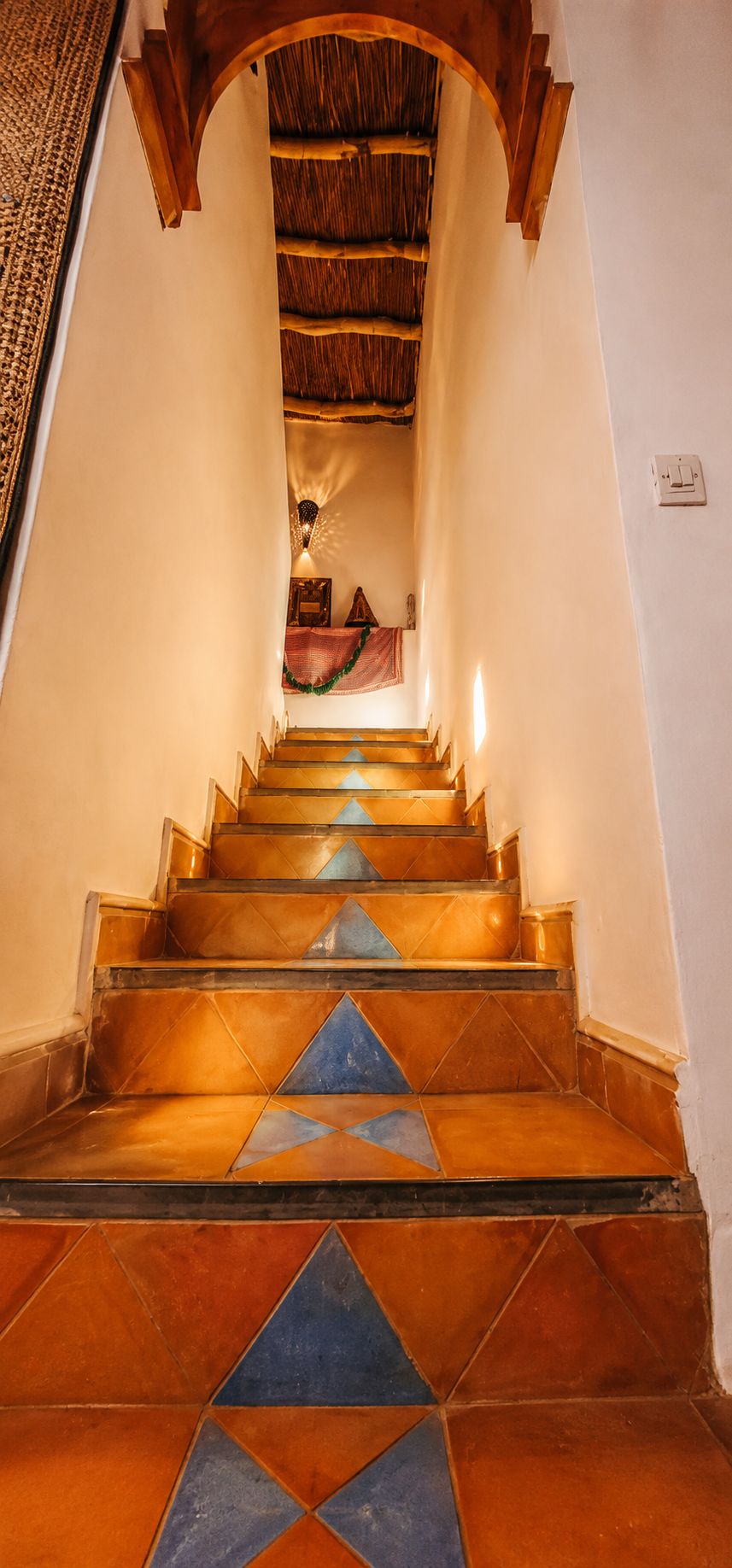 A staircase with a patterned floor leading to a room with a thatched ceiling.