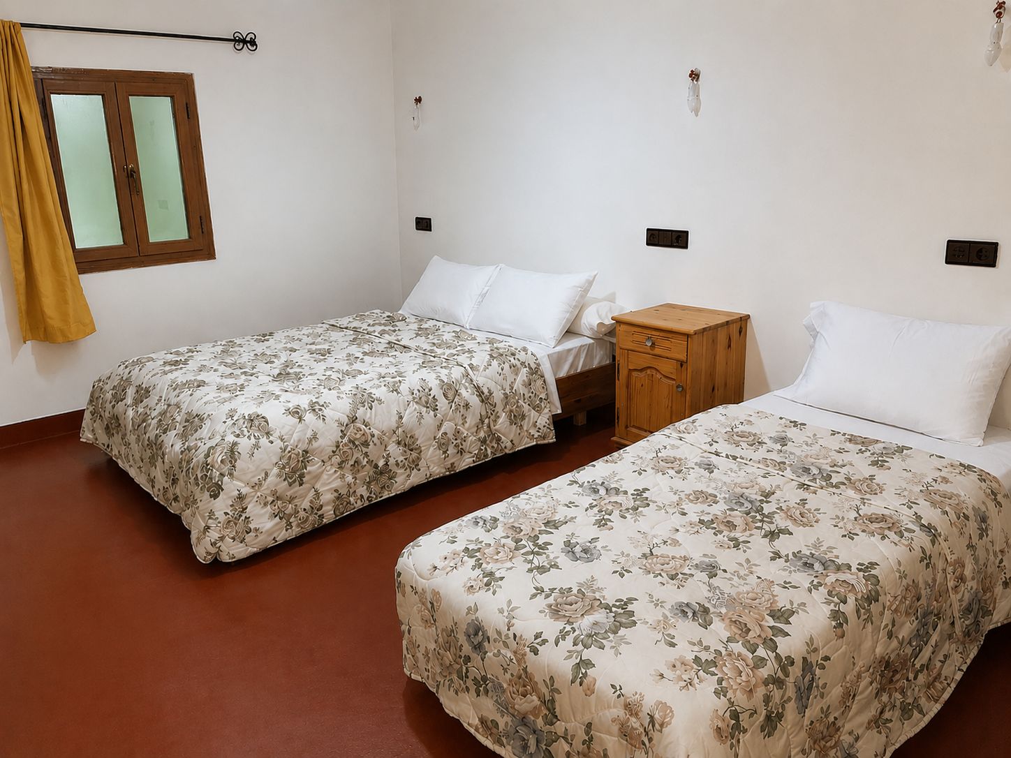 A bedroom with two single beds, a wooden nightstand, a wardrobe, and a window with curtains.