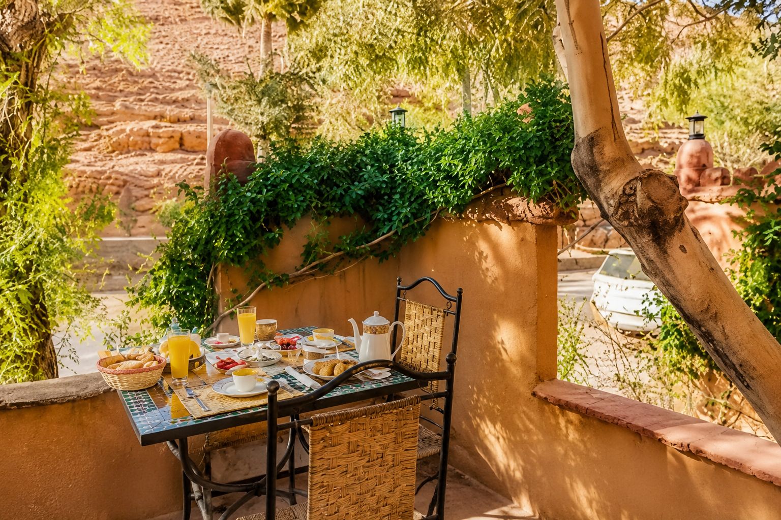 An outdoor dining area with a table set for breakfast, surrounded by greenery and a stone wall.