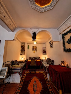 A room with a traditional design, featuring a central seating area with a sofa and chairs, a patterned rug, and a decorative ceiling.