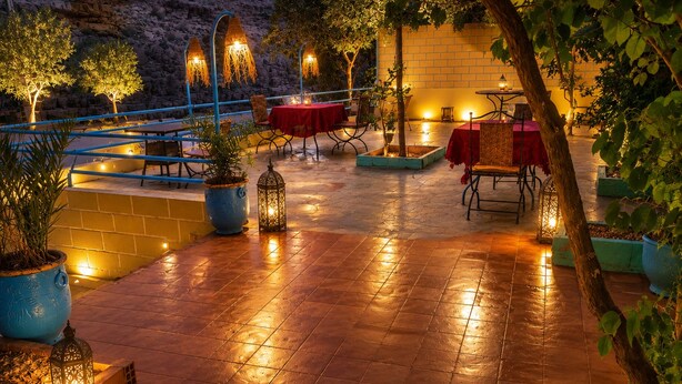 An outdoor patio area with tables and chairs, potted plants, and decorative lanterns. - Riad Kasbah des Roches (Drâa-Tafilalet)