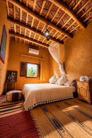 Una habitación con una cama, un mosquitero, un armario de madera y una ventana con cortinas.