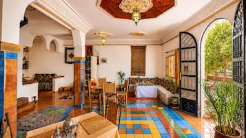 A traditional Moroccan interior with a tiled floor, a dining area with a table set for two, and a seating area with a sofa.