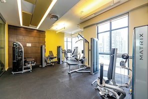 Ein Fitnessstudio mit verschiedenen Trainingsgeräten, großen Fenstern und Blick auf Gebäude.