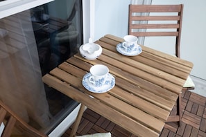 Ein Holztisch mit zwei weißen Tassen und Untertassen, einer weißen Schüssel und einem Holzstuhl.