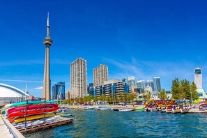 Eine Uferlandschaft mit einer markanten Turmstruktur, modernen Gebäuden und einem Yachthafen mit bunten Booten.