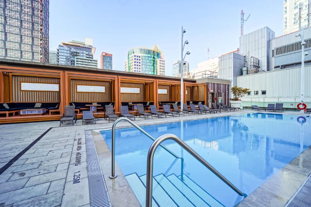 Piscina com espreguiçadeiras e paisagem urbana ao fundo.