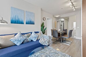 Un salon moderne avec un canapé bleu, des coussins à motifs, une table basse en verre et un coin repas comprenant des chaises et une table.