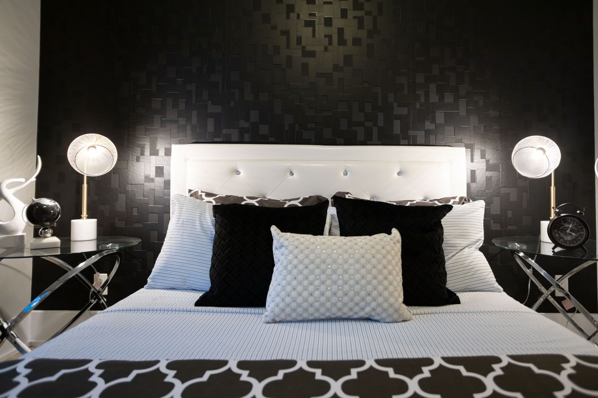 A modern bedroom with a tufted headboard, a patterned wall, and two bedside tables with lamps.