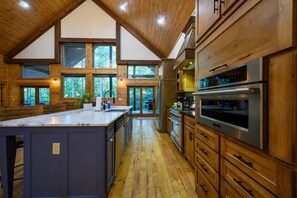 A spacious kitchen with wooden cabinets, a large island, and a view of the outdoors through multiple windows. - Luxury 5BR Cabin Near Broken Bow Lake with Hot Tub, Game Room & Playground (Broken Bow)