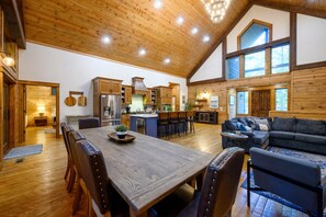 Una cocina amplia con armarios de madera y una isla grande, un comedor con mesa y sillas de madera, y una sala de estar acogedora con sofá y chimenea.
