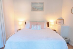 Cama bem arrumada com almofada estampada em listras que diz 'MEET ME AT THE BEACH'.