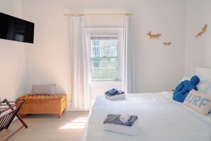 A hotel room with a bed, a small sofa, a TV mounted on the wall, and a window with curtains. - NEW! The Seabreeze! Fenced Backyard, Private Parking, King Bed, Pet Friendly (Wilmington)