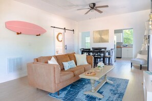 A modern living room with a sofa, coffee table, and a surfboard decoration. - NEW! The Seabreeze! Fenced Backyard, Private Parking, King Bed, Pet Friendly (Wilmington)