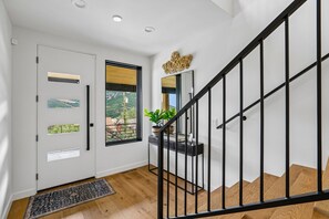 Um interior moderno com escada, porta com vista e uma pequena mesa com planta.