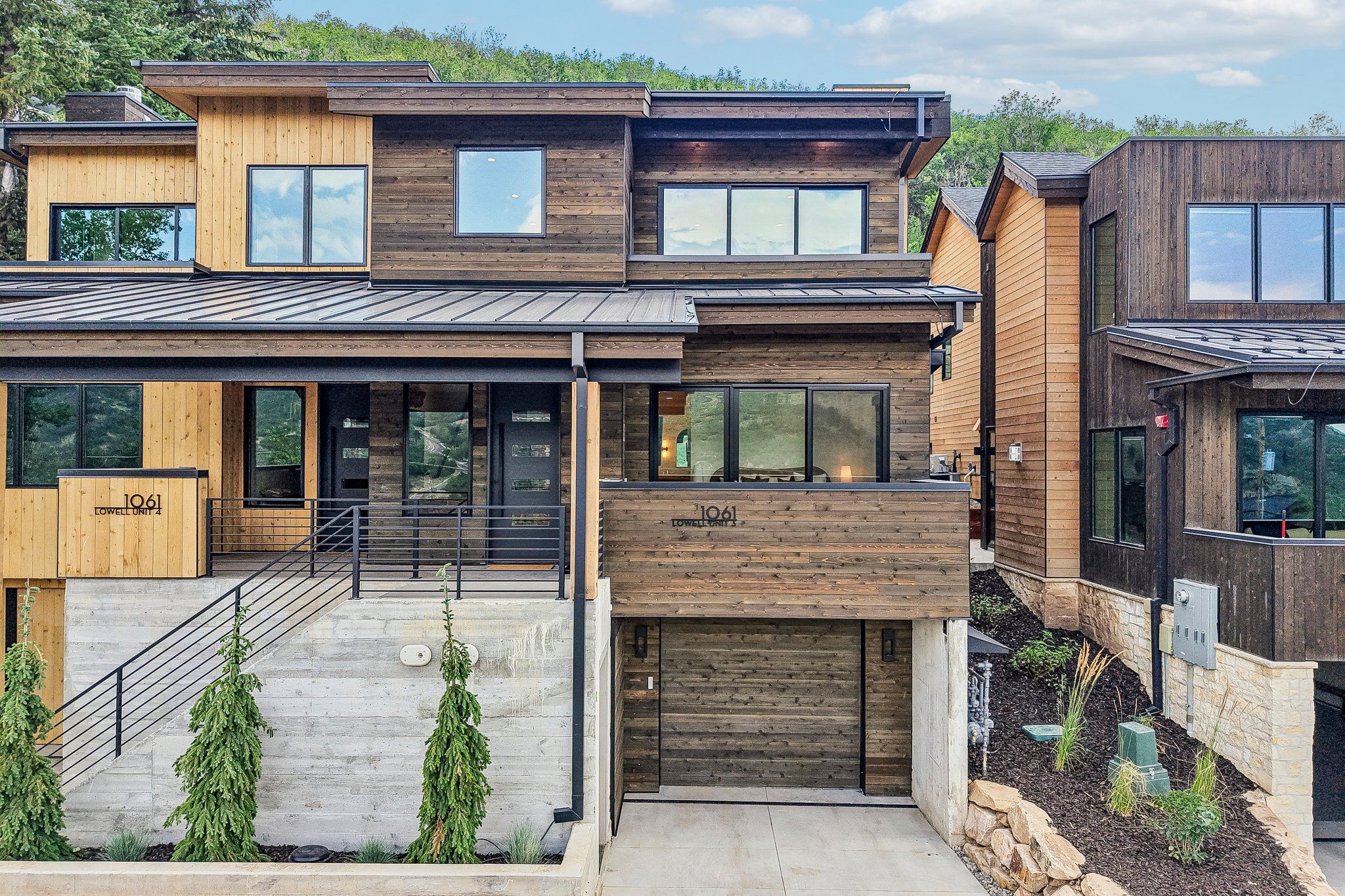 Ein modernes, mehrgeschossiges Haus mit einer Kombination aus Holz- und Metalleisten, großen Fenstern und einer sichtbaren Garagentür.