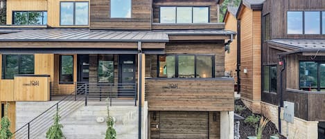 Ein modernes, mehrgeschossiges Haus mit einer Kombination aus Holz- und Metalleisten, großen Fenstern und einer sichtbaren Garagentür.