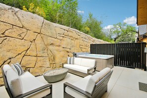 Eine Außenpatio mit einer Steinmauer, einem Whirlpool und einer Sitzecke mit Kissen und einer Schale mit Kieselsteinen.
