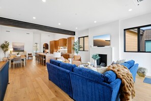 Ein modernes Wohnzimmer mit einem blauen Sofa, einem Kamin und einer Küche im Hintergrund.