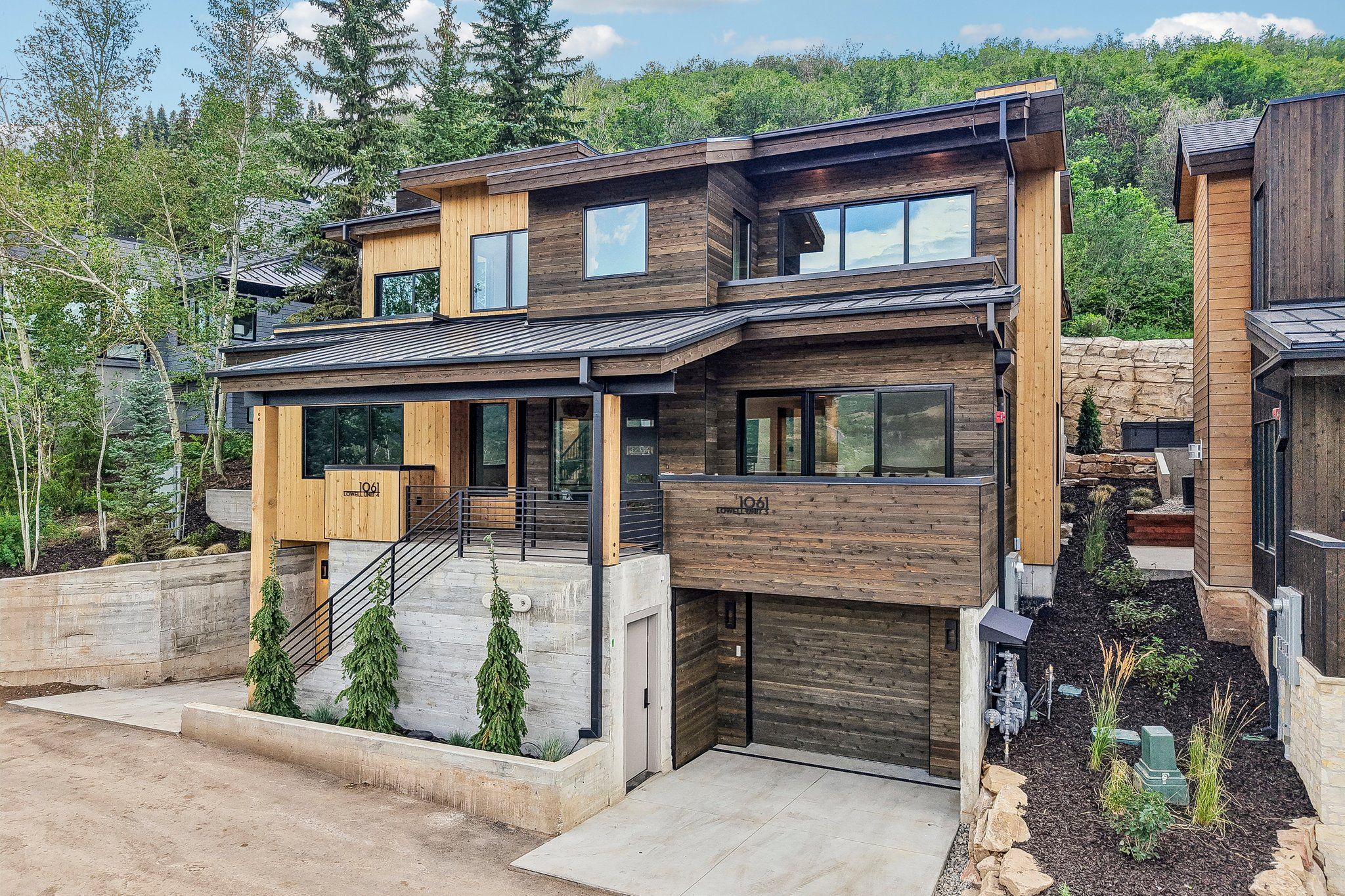 A modern two-story house with a garage, wooden exterior, and a small front yard.