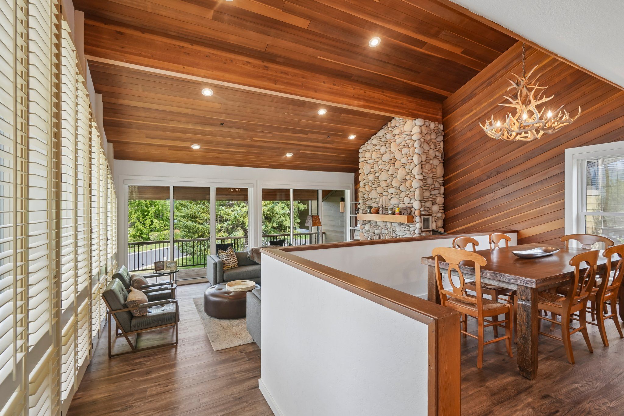 A modern kitchen with a stone wall, wooden ceiling, and a dining area with wooden chairs and a table.