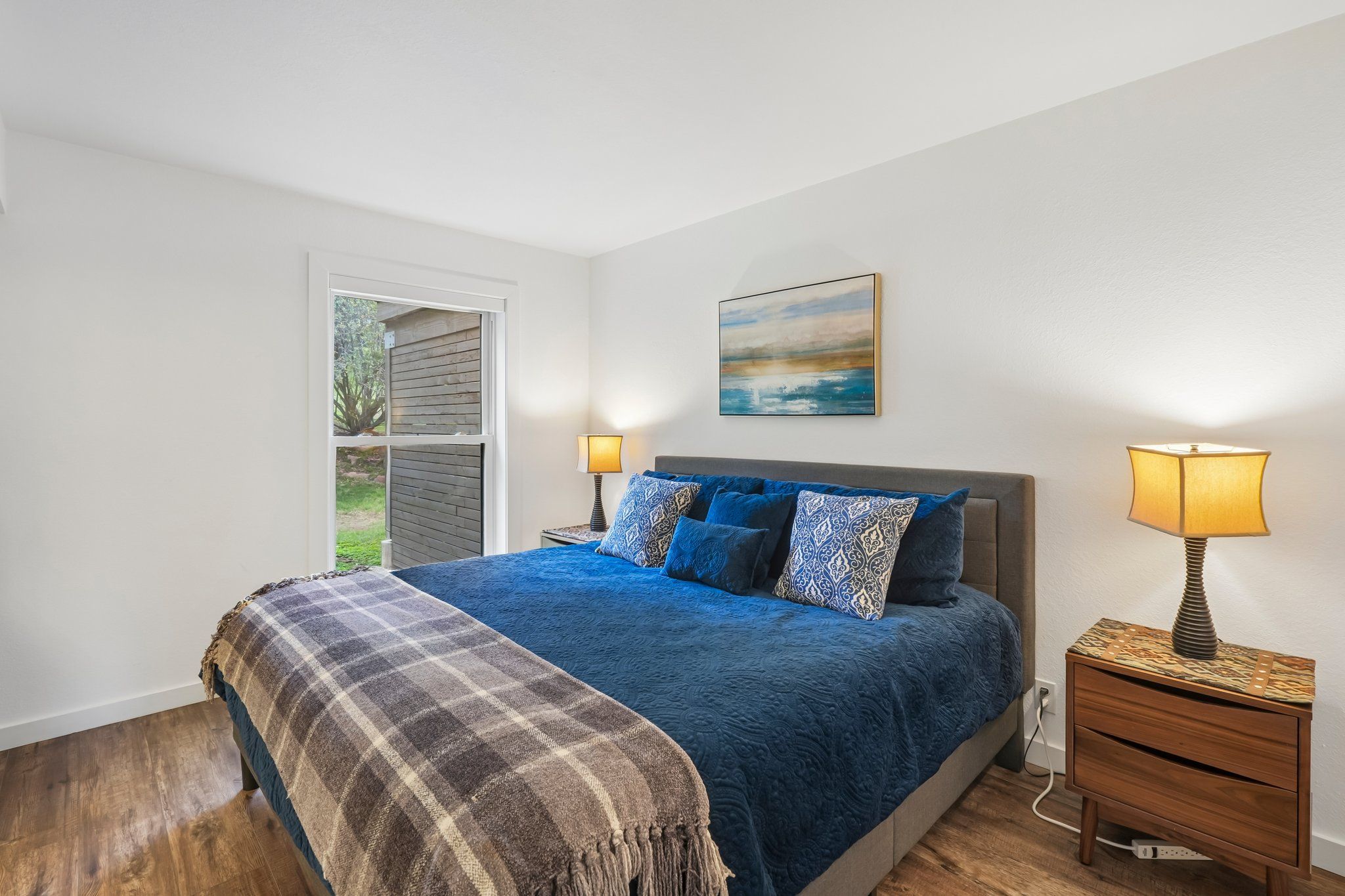 A bedroom with a bed, two bedside lamps, a painting, and a window.