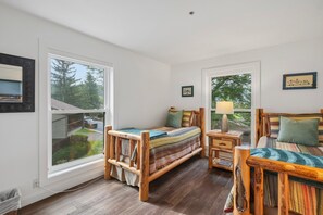 Ein Schlafzimmer mit zwei Holzbetten, einem Nachttisch mit Lampe und großen Fenstern mit Blick ins Freie.