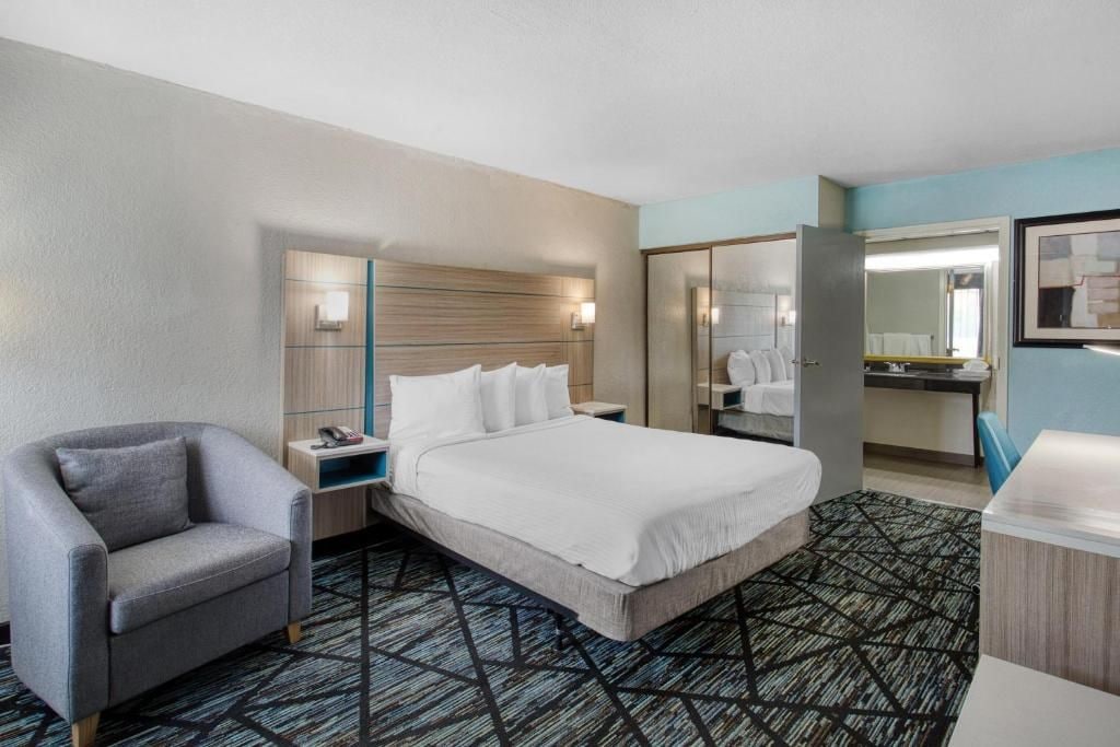 A hotel room with a bed, a chair, a desk, and a mirror.