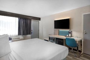 A hotel room with a bed, a desk with a chair, a flat-screen TV, and a minibar.